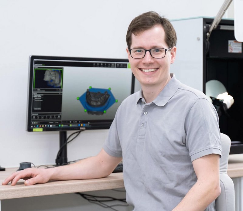 Zahntechniker sitzt an seinem Arbeitsplatz im Labor