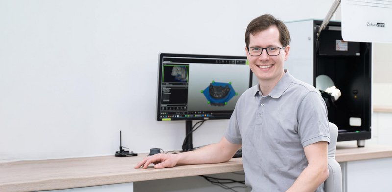 Zahntechniker sitzt an seinem Arbeitsplatz im Labor