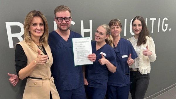 Fünf Zahnärzte stehen vor grauer Wand und einer hält ein Zertifikat hoch