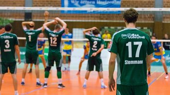 Handballspieler in grünen Trikots während eines Handballspiels in einer Sporthalle.