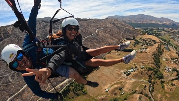 Tandem Gleitfliegen: Frau zeigt Peace-Zeichen in die Kamera