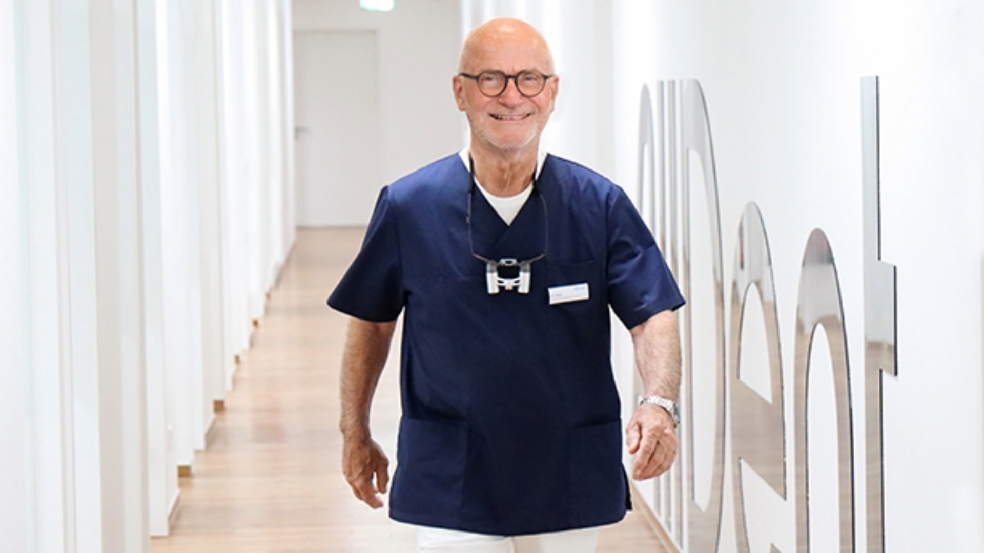 Chirurg läuft lächelnd durch den Praxisgang auf die Kamera zu