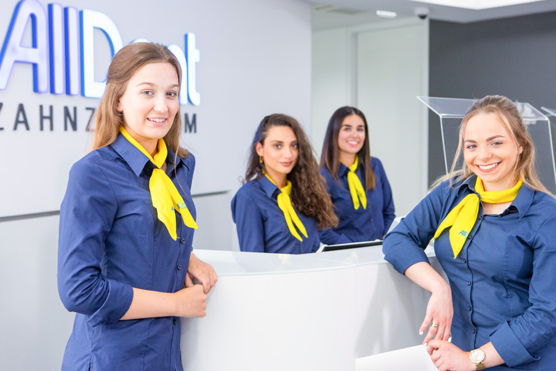 Empfangsteam steht am Tresen und lächelt in die Kamera