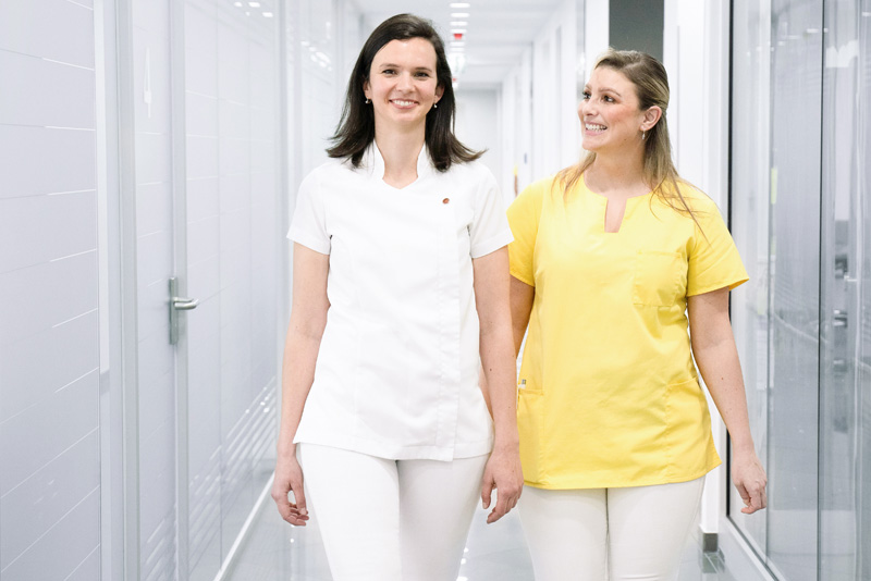 Zahnärztin und ZFA laufen nebeneinander durch den Gang der Praxis